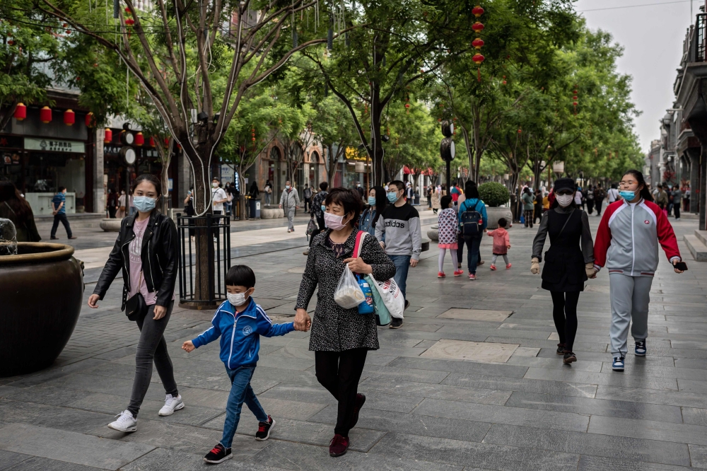 People wearing face masks as a preventive measure against the COVID-19 coronavirus walk on a street in Beijing on May 4, 2020. / AFP / NICOLAS ASFOURI