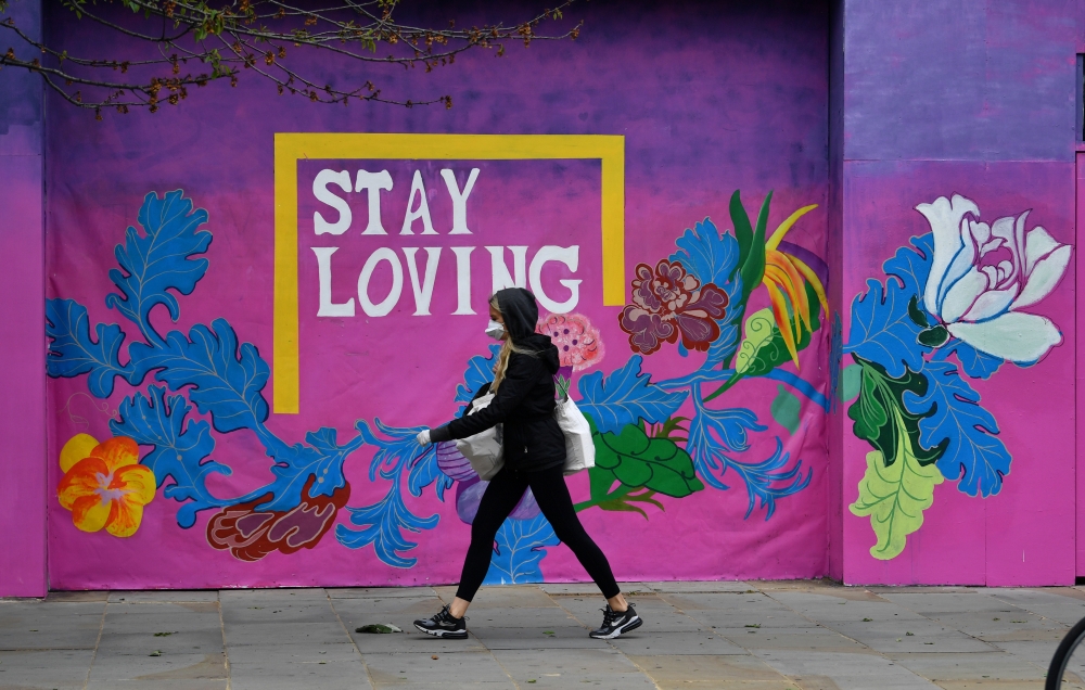 A woman wearing a protective face mask and gloves is seen walking past a mural, following the outbreak of the coronavirus disease (COVID-19), London, Britain, May 11, 2020. REUTERS/Dylan Martinez