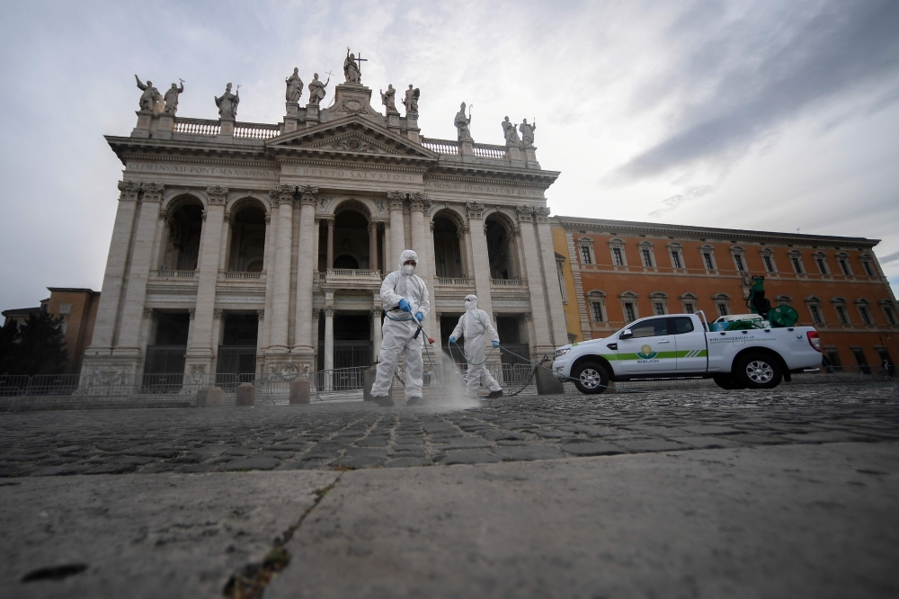 Employees of a disinfecting services company, wearing protective overalls and mask, sprays sanitizer on the forecourt during the sanitation of the Archbasilica of Saint John Lateran (San Giovanni in Laterano) in Rome on May 15, 2020  AFP / Filippo MONTEFO