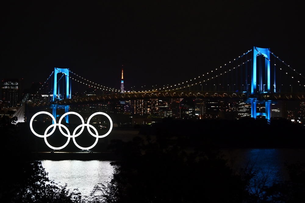 The Olympic rings, the Rainbow Bridge and the Tokyo Tower are seen at night in Tokyo on May 15, 2020. / AFP / CHARLY TRIBALLEAU