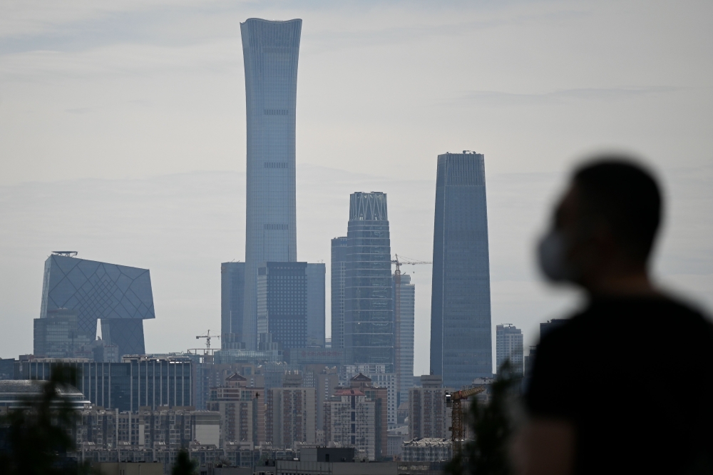 A man wearing a face mask looks at the skyline of the central business district (CBD) from a park in Beijing on May 23, 2020. / AFP / WANG ZHAO