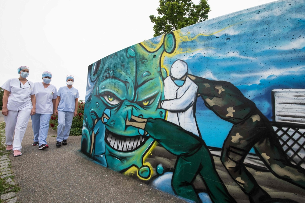 TOPSHOT - Medical staff members walk past a mural depicting a nurse, a doctor and a soldier fighting against the COVID-19 pandemic, painted by street artist Slimjoe in support of health workers, outside the Emilie Muller Hospital in Mulhouse, eastern Fran