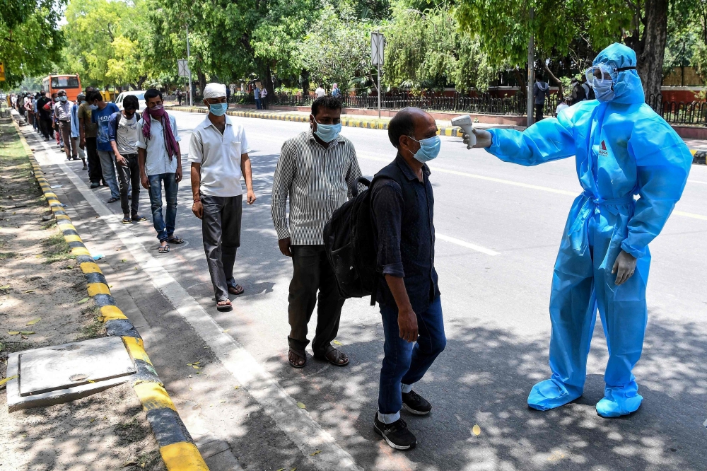 A volunteer wearing a protective suit checks the body temperature of homeless people standing in queue to get free lunch packets on the roadside after the goverment eased a nationwide lockdown as a preventive measure against the COVID-19 coronavirus, in N
