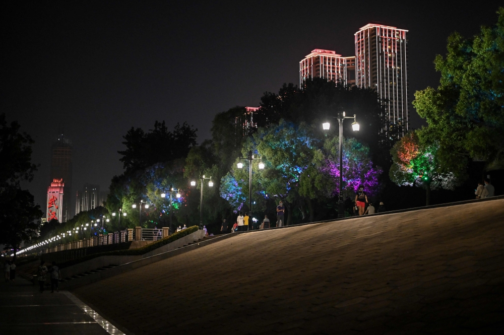 People wearing face masks walk along Hankou Park in Wuhan, in China's central Hubei province on May 28, 2020.  / AFP / Hector RETAMAL