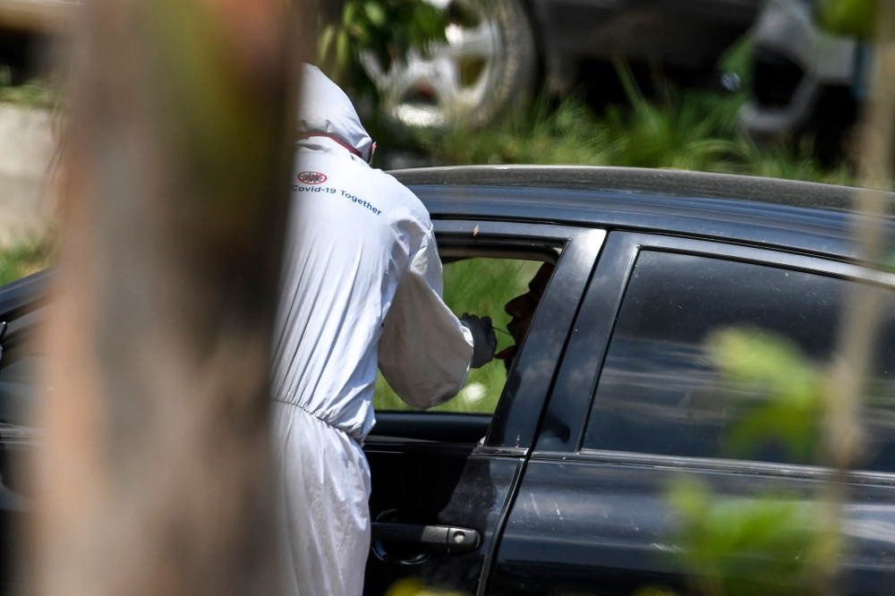 A health official (L) wearing protective gear takes a sample from a man sitting in a car at the drive-through screening and testing facility for the COVID-19 coronavirus alongside a street in Islamabad on June 3, 2020. / AFP / Aamir QURESHI
