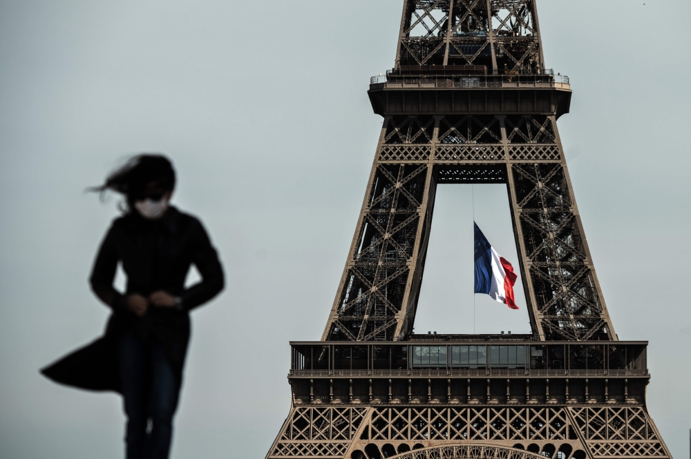 (FILES) In this file photo taken on May 11, 2020 a woman wearing a face mask walks as a French national flag flies on the Eiffel Tower in background in Paris on the first day of France's easing of lockdown measures in place for 55 days to curb the spread 