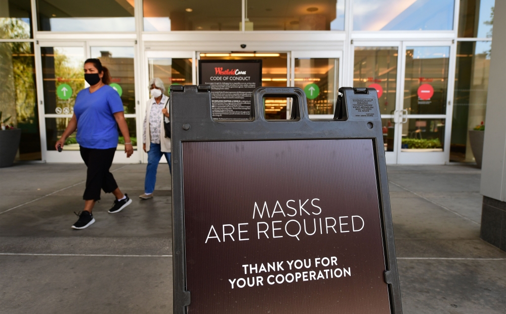 (FILES) In this file photo women wearing facemasks exit a shopping mall where a sign is posted at an entrance reminding people of the mask requirement Westfield Santa Anita shopping mall on June 12, 2020 in Arcadia, California, as Phase 3 in Los Angeles C