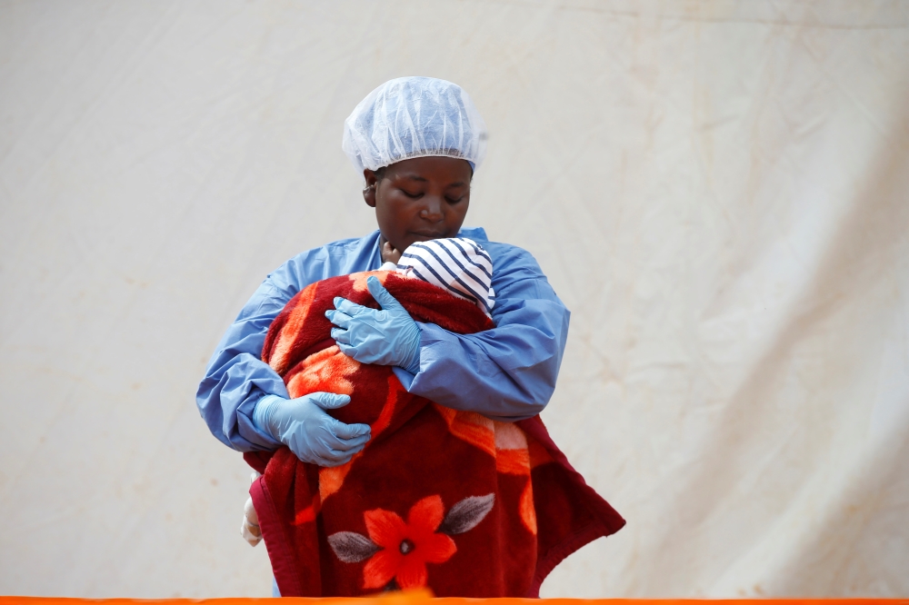Rachel Kahindo, an Ebola survivor working as a caregiver to babies who are confirmed Ebola cases, holds an infant outside the red zone at the Ebola treatment centre in Butembo, Democratic Republic of Congo, March 25, 2019. REUTERS/Baz Ratner/File Photo