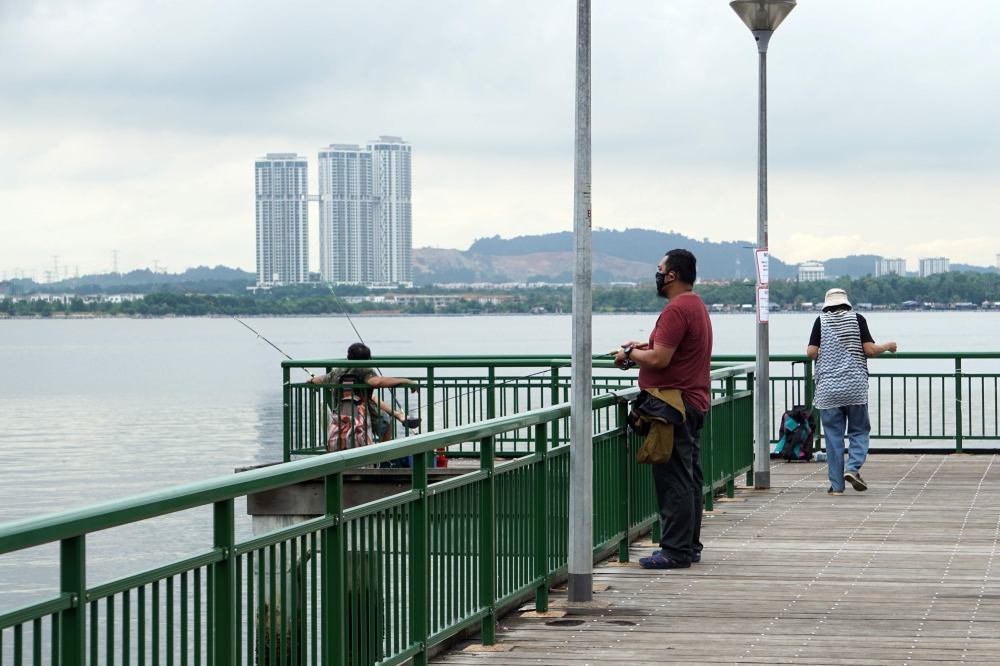 People fish from a jetty at a seafront in Singapore across Malaysia's southern state of Johor, seen in the background on June 23, 2020. / AFP / Roslan RAHMAN