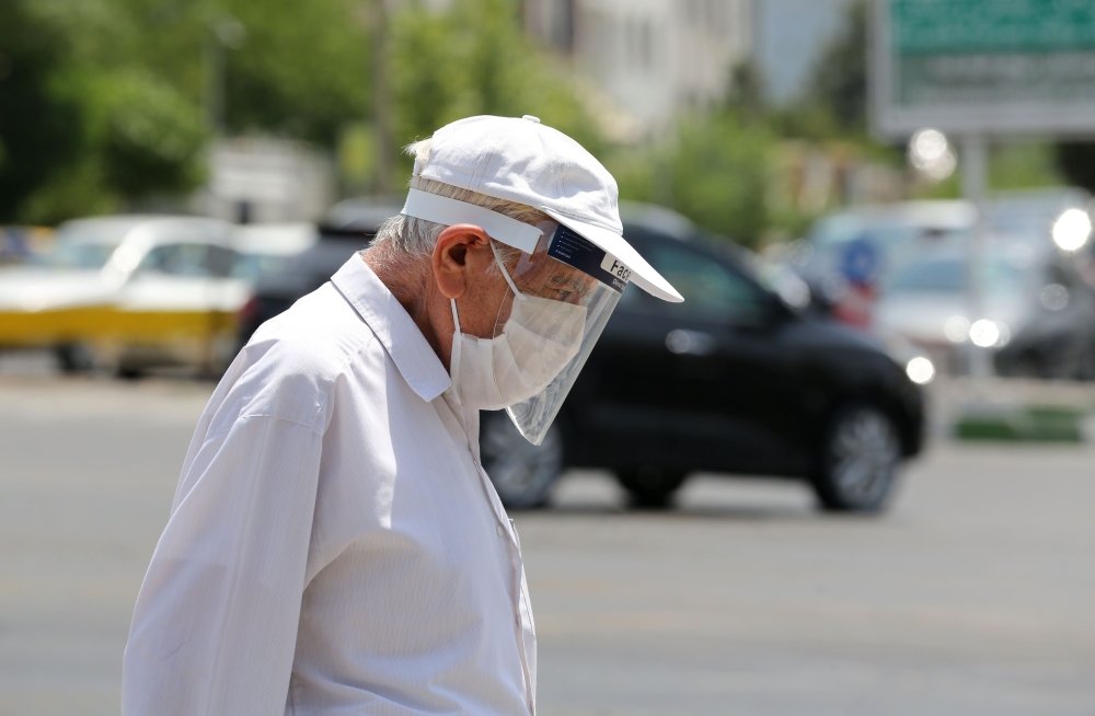 A pedestrian wearing a protective mask and a shield due to the COVID-19 coronavirus, walks along a street in the Iranian capital Tehran on June 28, 2020. AFP / ATTA KENARE
