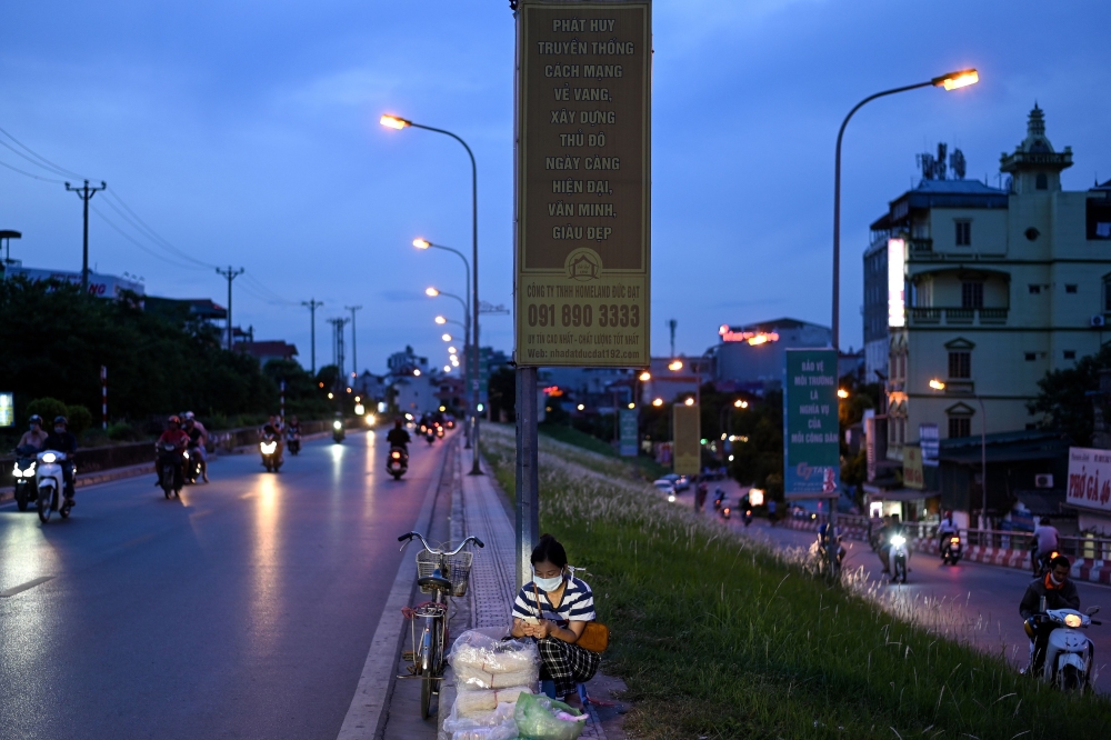 A vendor selling rice noodles waits for customers along a street at sunset in Hanoi on July 9, 2020. / AFP / Manan VATSYAYANA