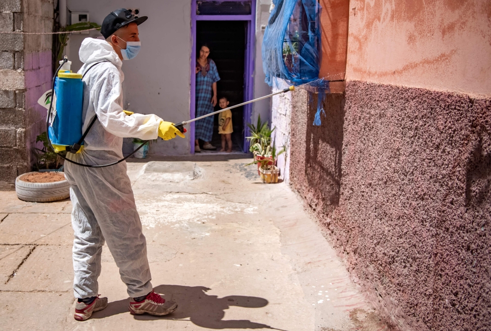 A woman and a child confined at home watch a Moroccan municipal worker disinfect their street in the southern port city of Safi on June 9, 2020, during a total lockdown ordered by the authorities following the discovery of several new cases of COVID-19 co