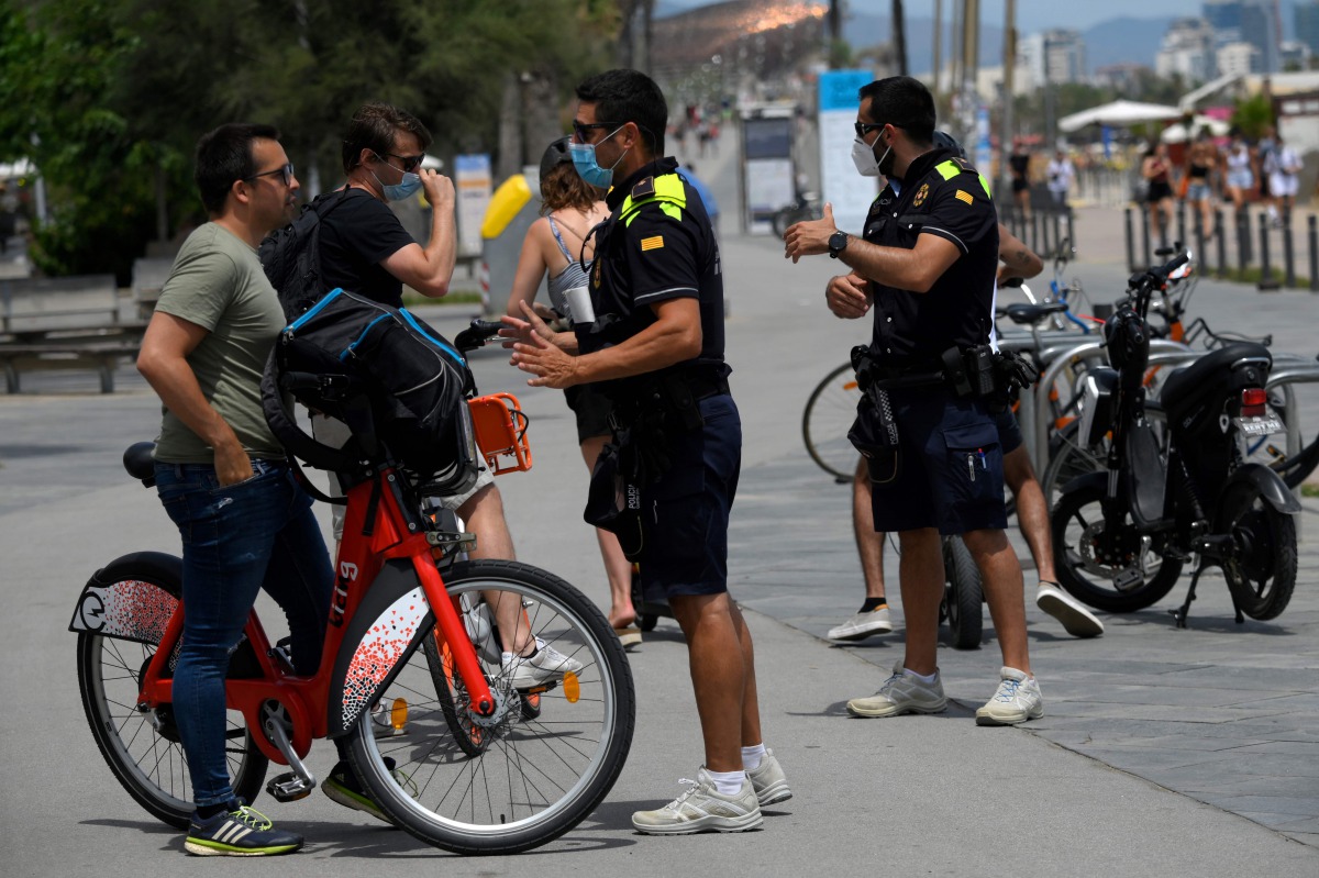 Catalan municipal police officers ask citizens to wear face masks at Barceloneta Beach in Barcelona on July 9, 2020. Regional officials in Catalonia said they want to toughen the existing rules to make wearing masks compulsory in public, to stem a rising 
