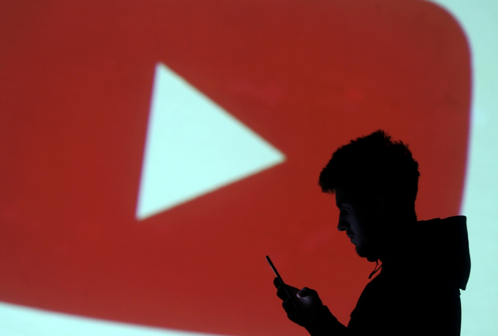 FILE PHOTO: A silhouette of a mobile user is seen next to a screen projection of Youtube logo in this picture illustration taken March 28, 2018. REUTERS/Dado Ruvic/File Photo