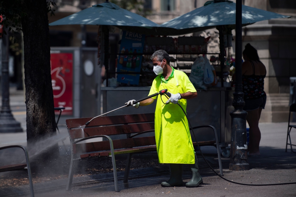 A municipal worker cleans a bench at Catalonia square in Barcelona on July 18, 2020. Four million residents of Barcelona have been urged to stay at home as virus cases rise, while EU leaders were set to meet again in Brussels, seeking to rescue Europe's e