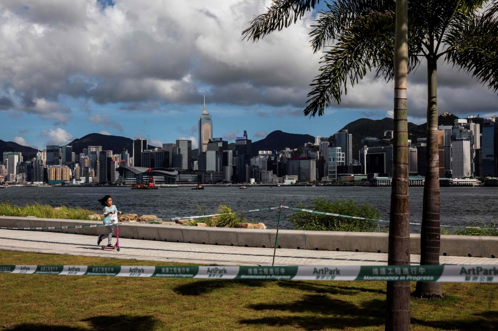 A girl (L) rides her scooter at the west kowloon cultural district in Hong Kong on July 18, 2020. / AFP / ISAAC LAWRENCE
