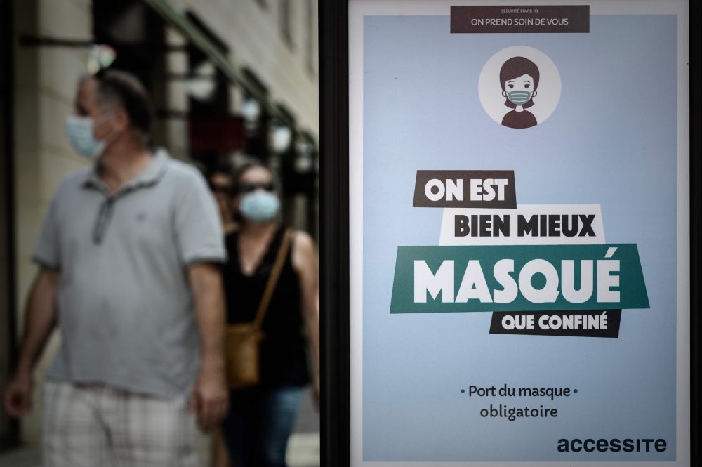A man and a woman wearing protective face masks due to the COVID-19 coronavirus pandemic, walk past a mandatory wearing mask sign, in Bordeaux, southwestern France, on July 18, 2020. / AFP / Philippe LOPEZ