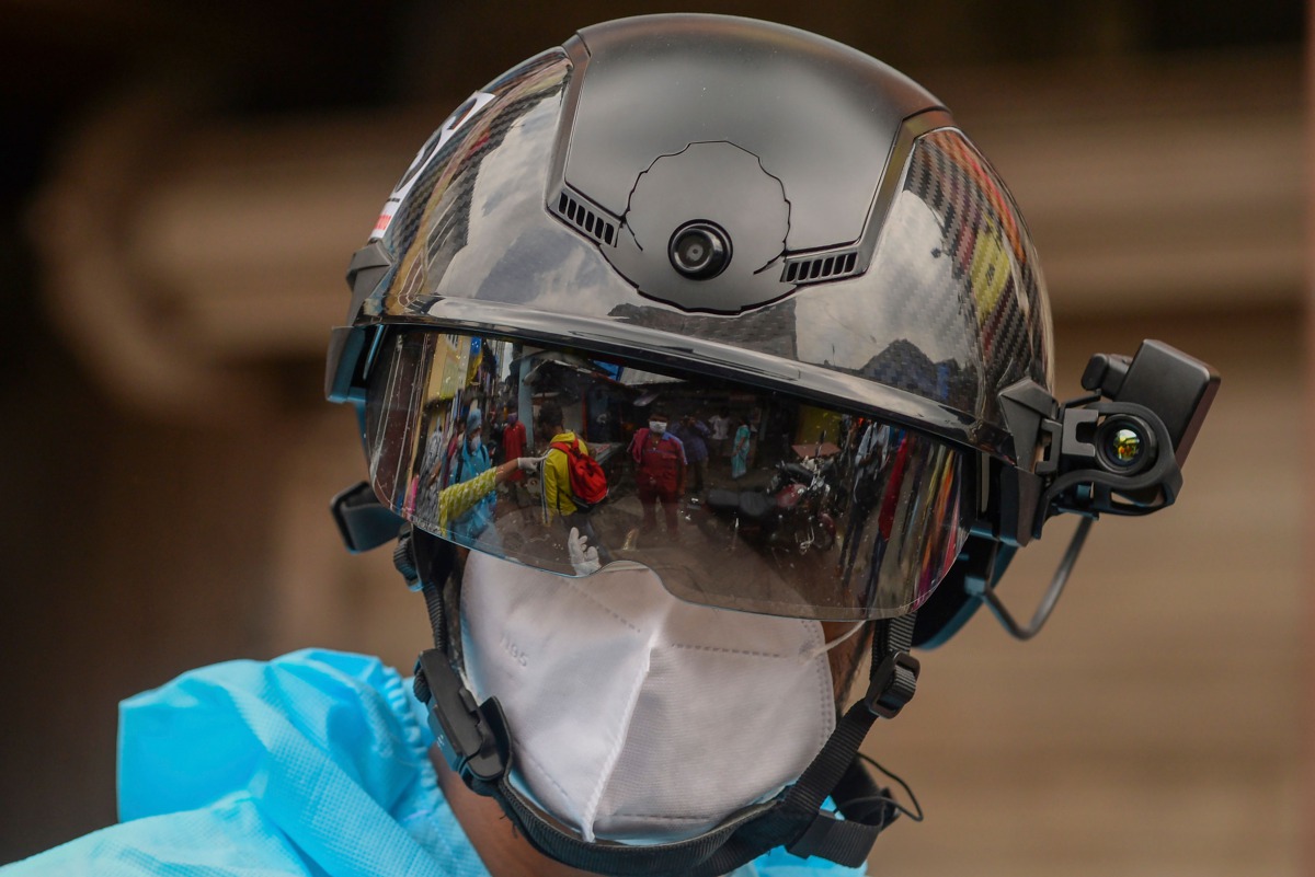 A volunteer health worker of the Non-Governmental Organization (NGO) Bharatiya Jain Sanghatana (BJS) wearing Personal Protective Equipment (PPE) looks through a smart helmet equipped with a thermo-scan sensor to check the body temperature during a door-to