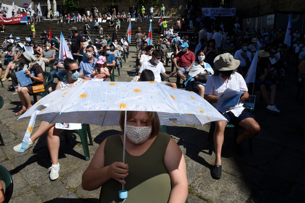 A woman holds an umbrella to protect herself from the sun as protesters respect social distancing measures during a demonstration by independence supporters in Santiago de Compostela on July 25, 2020. / AFP / MIGUEL RIOPA