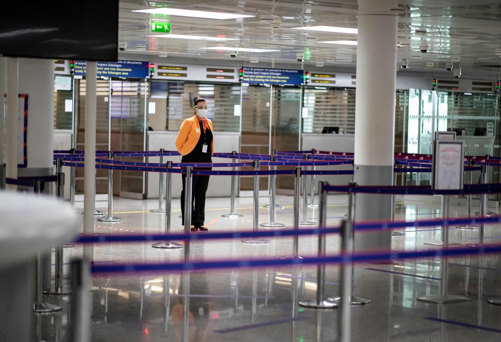 (FILES) In this file photo taken on May 14, 2020 a member of Charles de Gaulle airport personnel wears a protective face mask in the deserted passport control section of arrivals in Terminal 2 of Charles de Gaulle international airport in Roissy near Pari