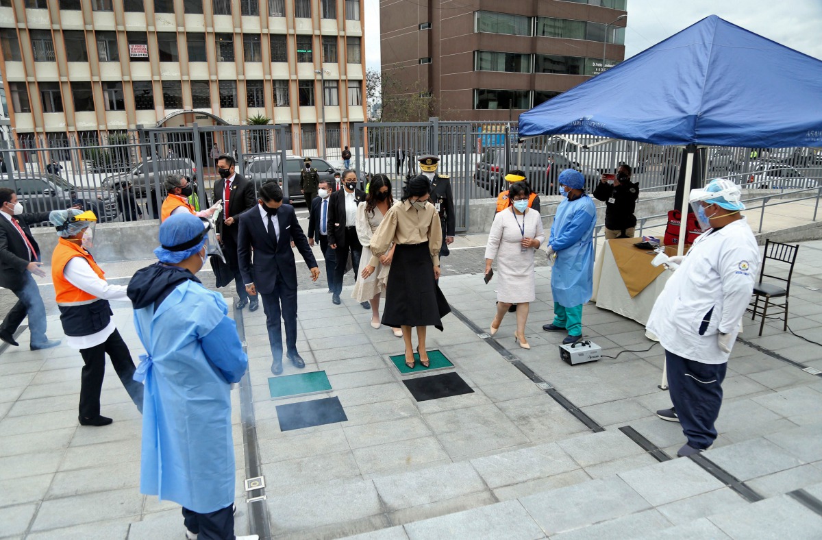 Handout picture released by Ecuador's National Assembly showing the new Vice-President of Ecuador, Maria Alejandra Munoz (C) disinfection her shoes against the spread of the COVID-19 novel coronavirus upon arriving at her inauguration at the National Asse
