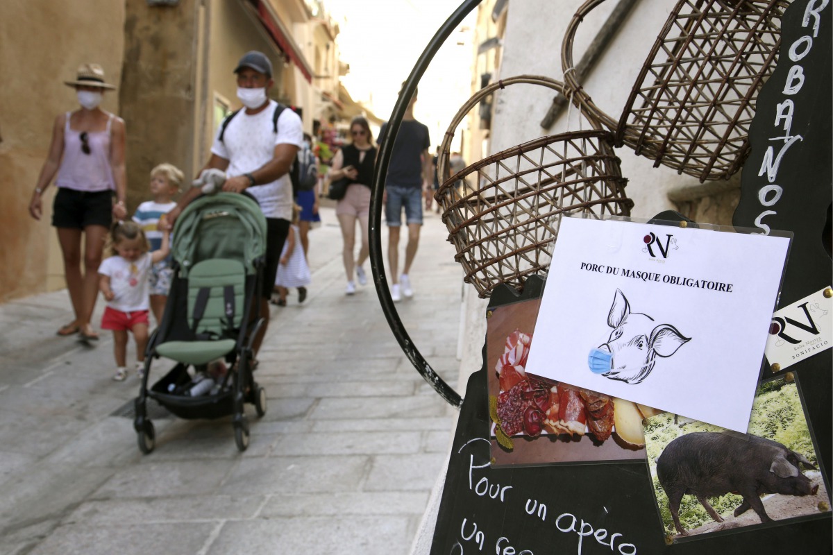 Tourists with protective masks walk past a sign reading 'mask is mandatory' in the streets of the old city of Bonifacio on August 5, 2020 on the French Mediterranean island of Corsica, the first and only city in Corsica where the mask is mandatory in the 