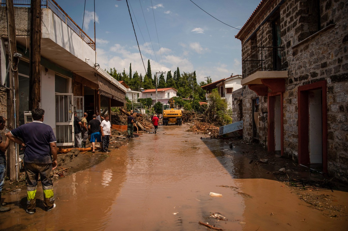 People clean in a destroyed street following a storm at the village of Politika, on Evia island, northeast of Athens, on August 9, 2020. Five people including a baby died and two more were missing as torrential rains and floods swept the Greek island of E