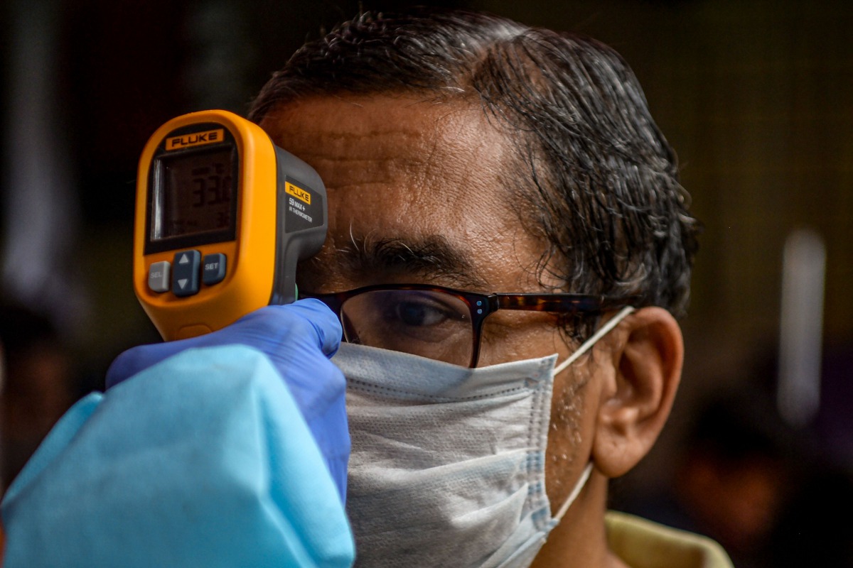A health worker checks the body temperature of a resident during a COVID-19 coronavirus screening in Mumbai on August 12, 2020. / AFP / INDRANIL MUKHERJEE