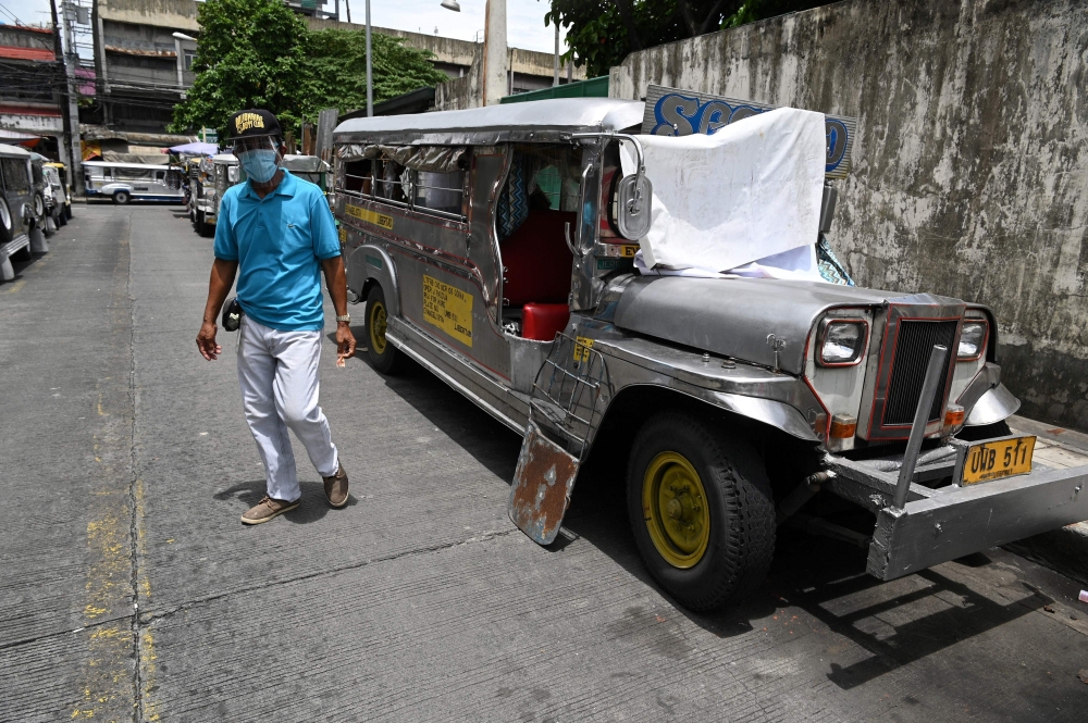 In this photo taken on August 12, 2020, a resident walks past jeepneys serving as temporary homes parked along a road in Manila. FOCUS by Ron LOPEZ / AFP / Ted ALJIBE 