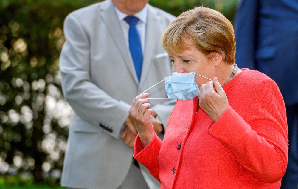 German Chancellor Angela Merkel takes off her face mask as she arrives for a family photo in front of the Staendehaus former parliament building prior to a North Rhine-Westphalian cabinet meeting on August 18, 2020 in Duesseldorf, western Germany. / AFP /