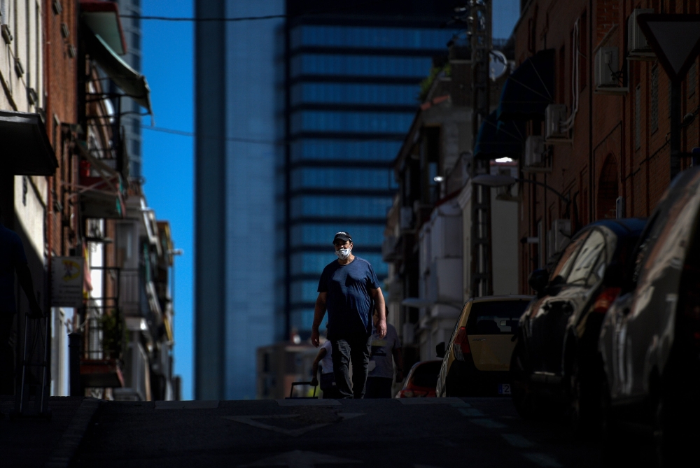 A man wearing a facemask walks in the outskirts of Madrid on August 19, 2020, with the Cuatro Torres bussiness area in the background. / AFP / OSCAR DEL POZO
