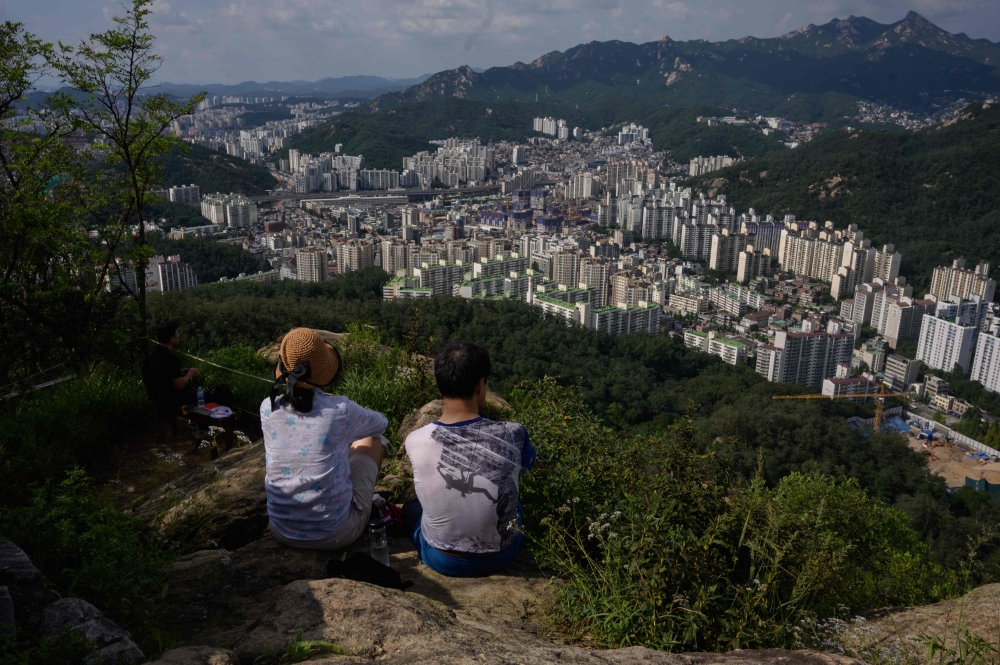 Hikers sit at a viewpoint overlooking the Seoul city skyline on August 23, 2020. South Korea ramped up coronavirus restrictions on August 23 to try to contain a growing outbreak, as many countries around the world battled worrying surges in infections. / 