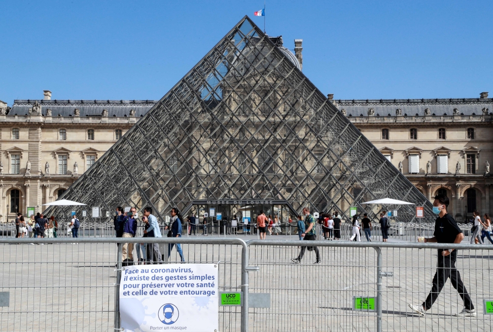 People wearing face masks walk in front of the Louvre Pyramid (Pyramide du Louvre) designed by Ieoh Ming Pei, at the Cour Napoleon, in Paris, on August 27, 2020.  AFP / Ludovic MARIN / 