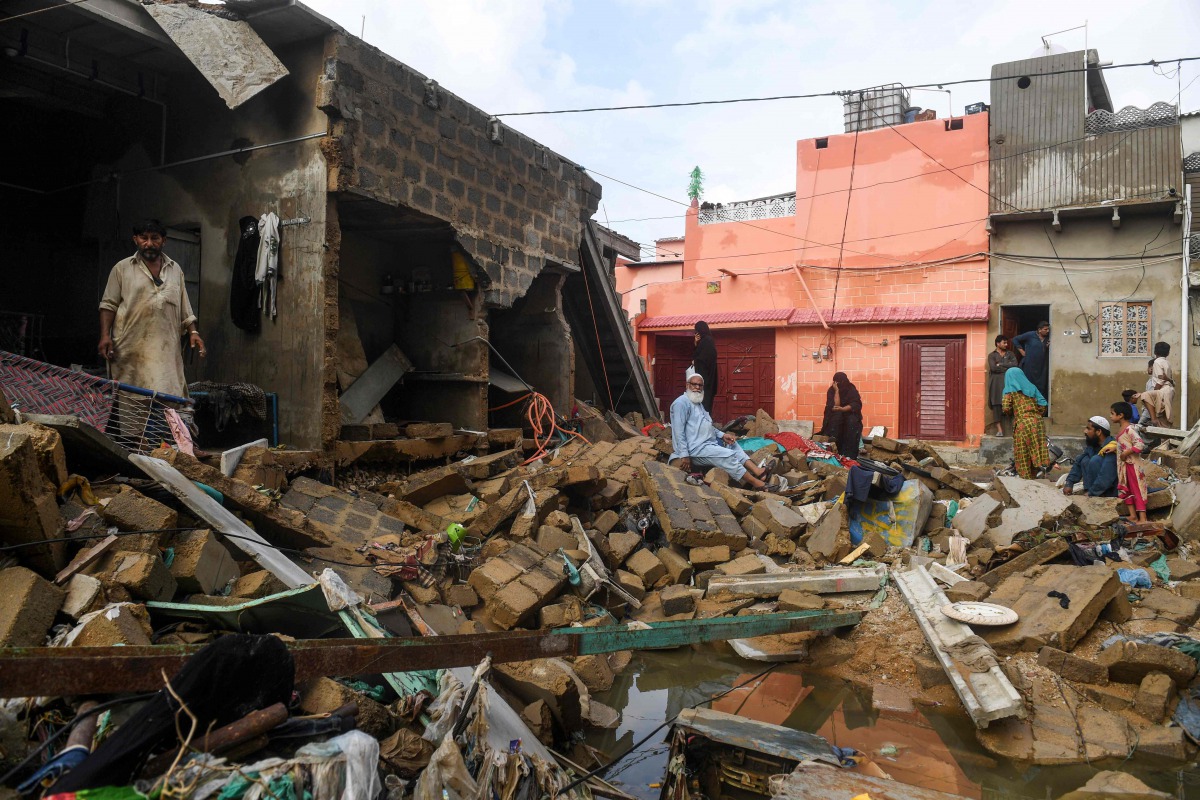 Residents sit over the debris of their collapsed houses at a flooded residential area after heavy monsoon rains in Pakistan's port city of Karachi on August 26, 2020. Heavy monsoon rains have also wrought havoc on neighbouring Pakistan, with authorities i