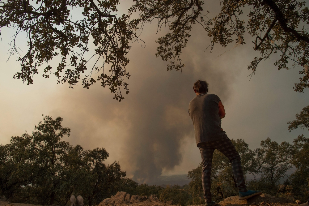 A resident observes a wildfire raging near El Buitron in Huelva on August 30, 2020. At least 3,200 people were evacuated because of a fire that has already ravaged some 10,000 hectares in the southwestern Spanish province of Huelva and which remains activ
