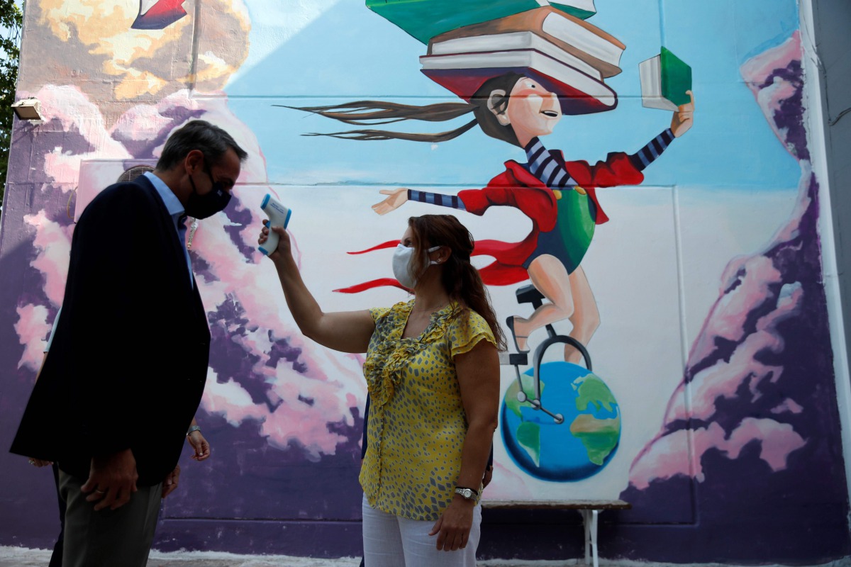A teacher takes the temperature of Greece's Prime Minister Kyriakos Mitsotakis as he arrives at a primary school on the first day of class of the new academic year in ATHENS, on September 14, 2020. Schools open on Monday amid concerns due to a new spike i