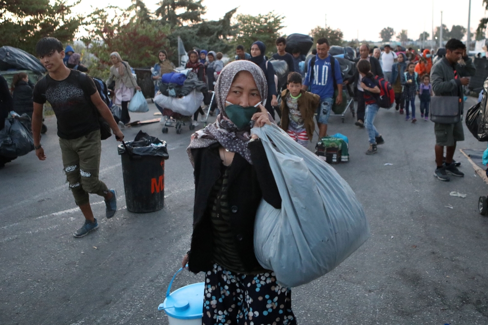 Refugees and migrants from the destroyed Moria camp carry their belongings as they walk towards a new temporary camp, on the island of Lesbos, Greece, September 18, 2020. REUTERS/Elias Marcou