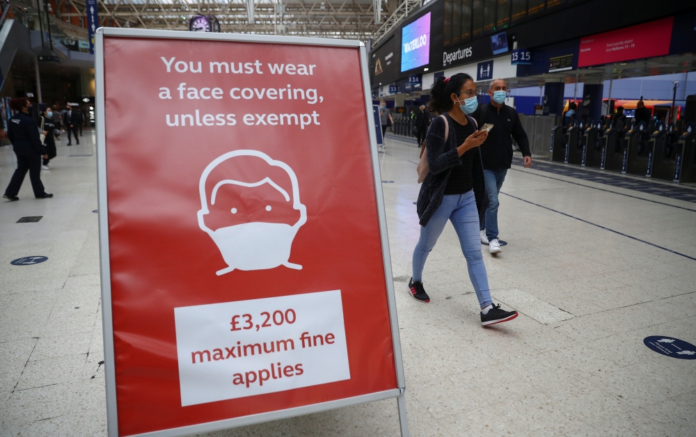 People wearing protective face masks pass a sign at Waterloo station during the morning rush hour, amid the coronavirus disease (COVID-19) outbreak, in London, Britain, September 23, 2020. REUTERS/Hannah McKay