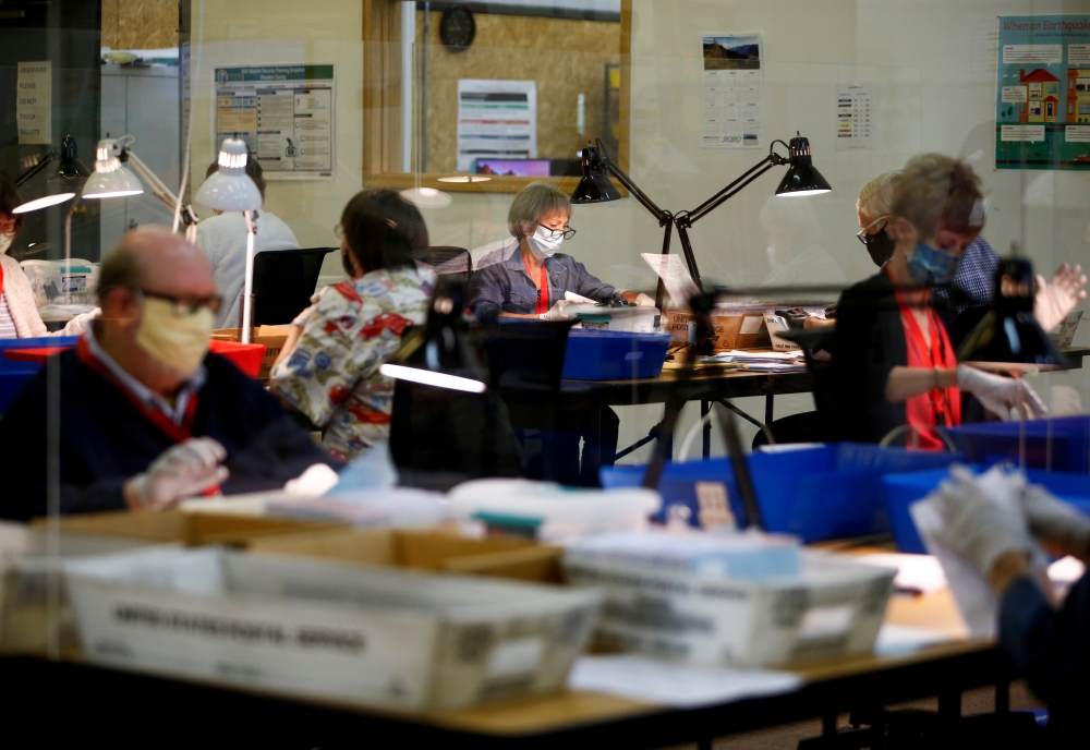 FILE PHOTO: Workers wearing masks and separated by plexiglass inspect ballots at the Thurston County Ballot Processing Center in Tumwater, Washington, U.S. July 23, 2020. REUTERS/Lindsey Wasson
