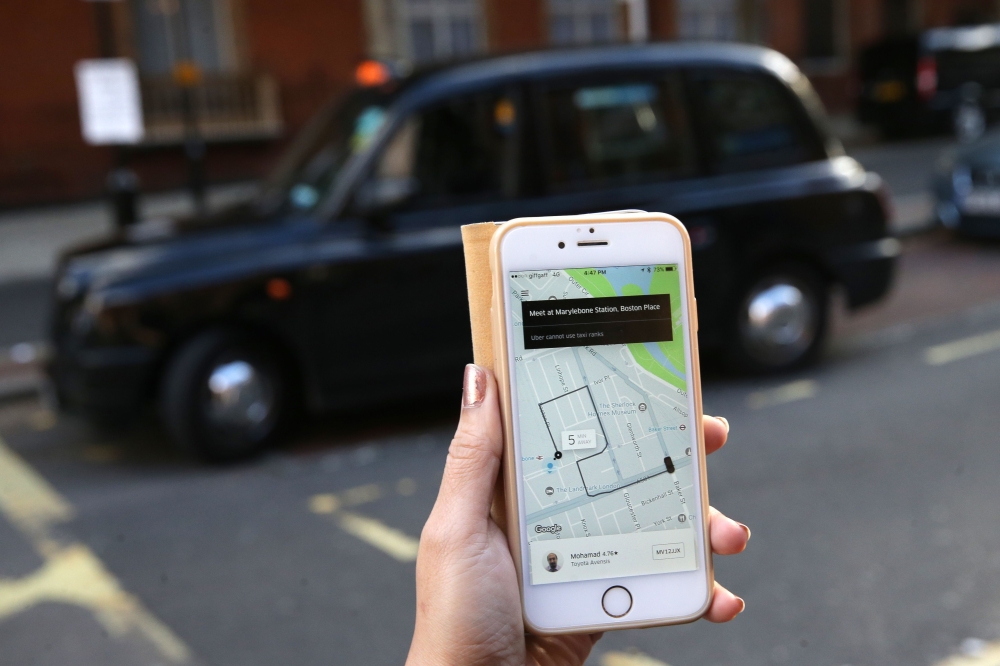 A woman poses holding a smartphone showing the App for ride-sharing cab service Uber in London.  AFP / Daniel LEAL-OLIVAS