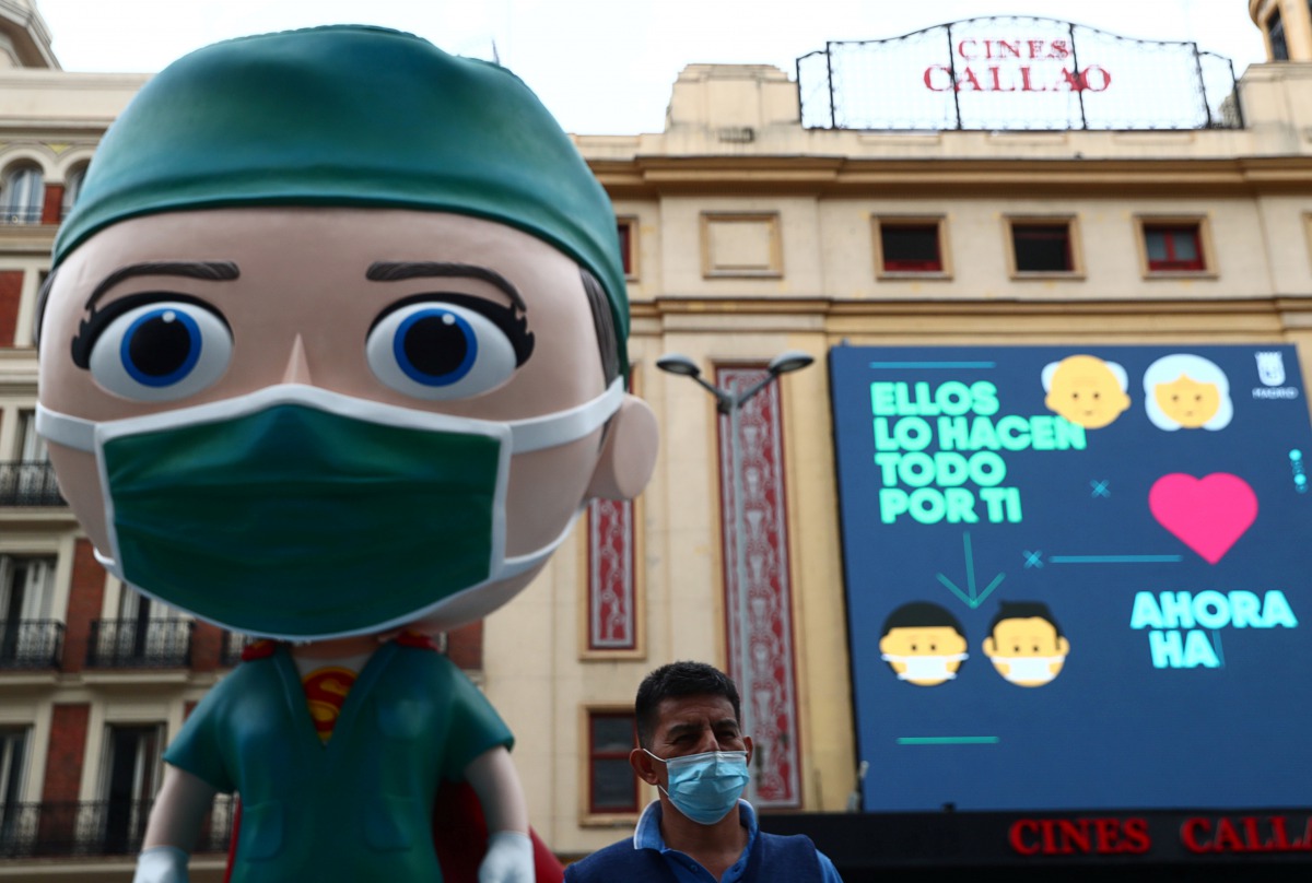 A man wearing a protective face mask poses for a picture next to an oversized model of a health worker amid the outbreak of the coronavirus disease (COVID-19), in Madrid, Spain September 24, 2020. REUTERS/Sergio Perez
