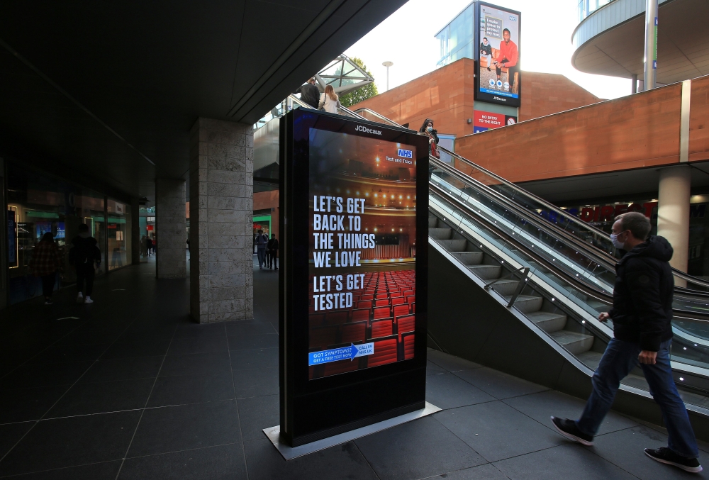 A man wearing a face mask or covering due to the COVID-19 pandemic, walks past a digital sign advising pedestrians of the Government's latest coronavirus guidance, in Liverpool, north west England on October 1, 2020, as Britain's Health Secretary Matt Han