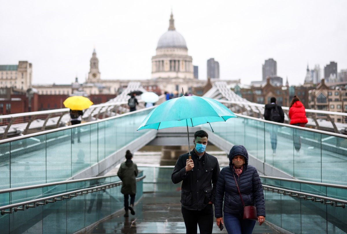 People walk across Millennium Bridge during rainy weather, in LONDON, Britain, October 4, 2020. REUTERS/Henry Nicholls
