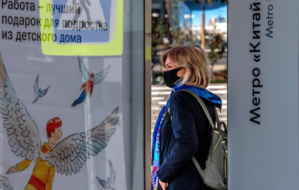 A woman wearing a face mask to protect against the coronavirus disease stands at a bus stop in central Moscow on October 5, 2020. / AFP / Yuri KADOBNOV