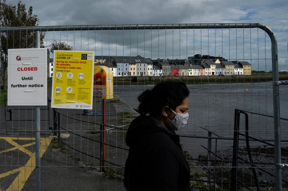 Houses are seen as a woman wearing a protective face mask walks past a closed main walkway as the National Public Health Emergency Team (NPHET) announced recommendations that the government implement the highest level of COVID-19 restrictions to Level 5, 