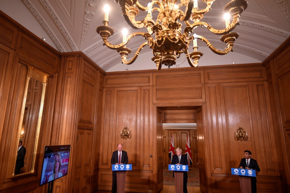 Britain's Prime Minister Boris Johnson, Chancellor of the Exchequer, Rishi Sunak and Chief Medical Officer for England, Chris Whitty listen to a question of Laura Kuenssberg (on screen) as the attend a virtual news conference on the ongoing situation with