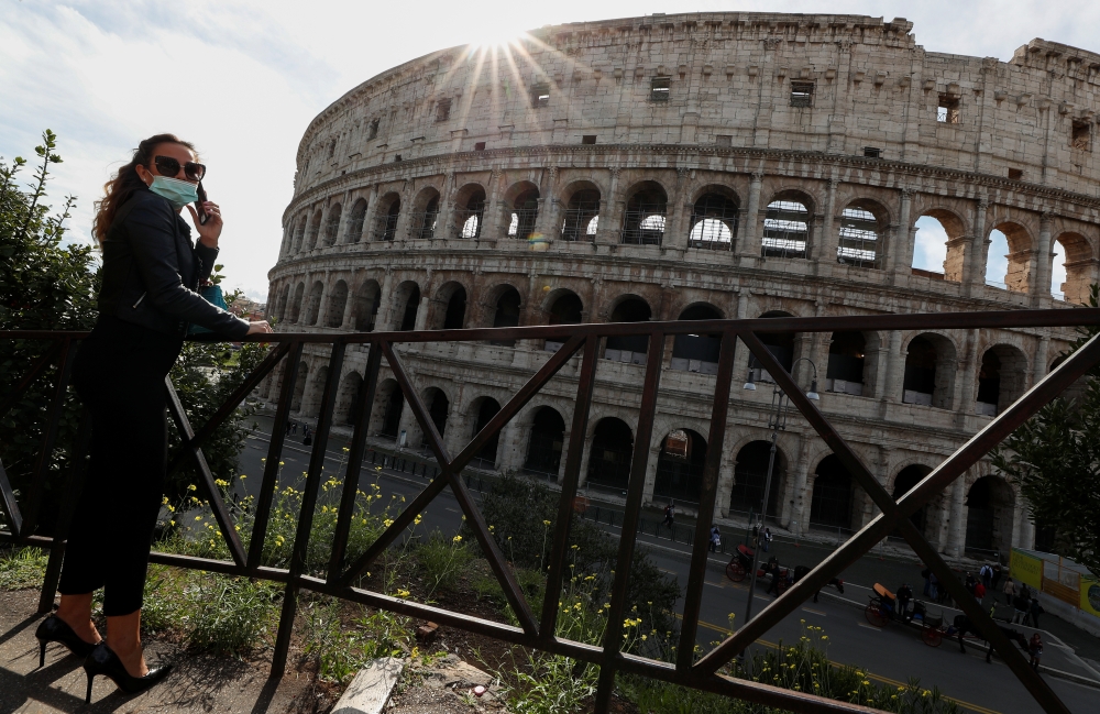 A woman wearing a face mask stands next to the Colosseum as Italy adopts new restrictions aimed at curbing a surge in the coronavirus disease (COVID-19) infections, in Rome, Italy October 13, 2020. Reuters/Guglielmo Mangiapane