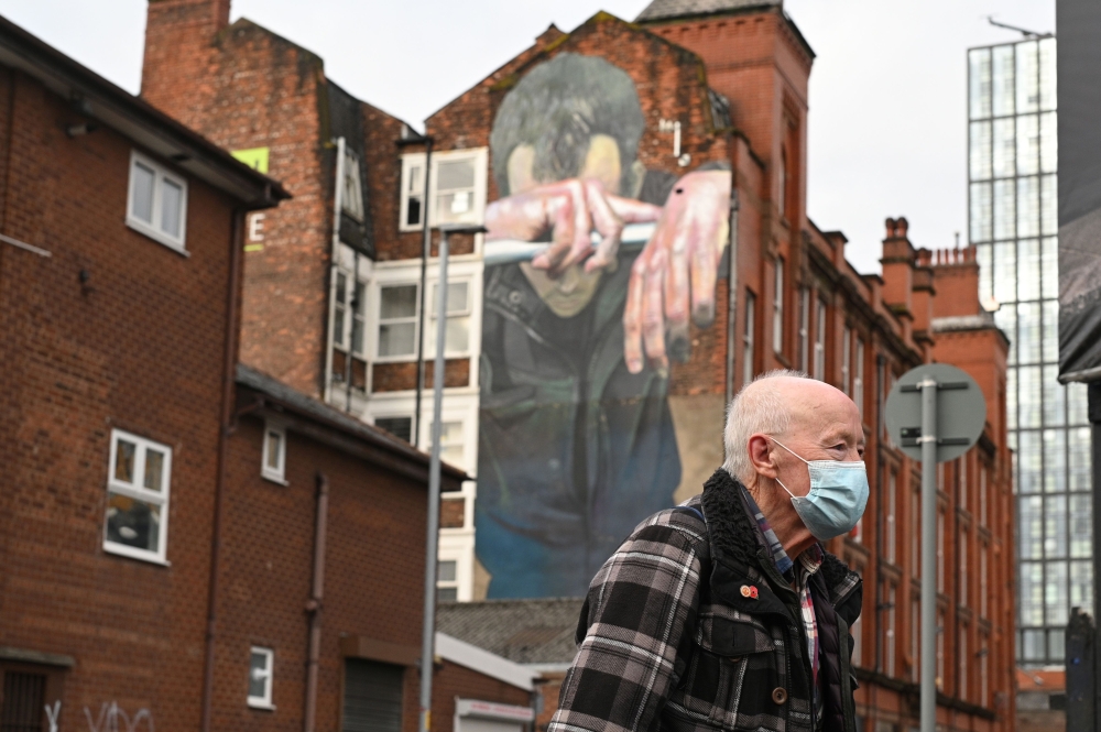 A man wearing a facemask walks past a mural painted as part of the Cities of Hope festival in 2016 and highlighting the effects of mental health, in Ancoats, northern Manchester on October 16, 2020, as the number of cases of the novel coronavirus COVID-19