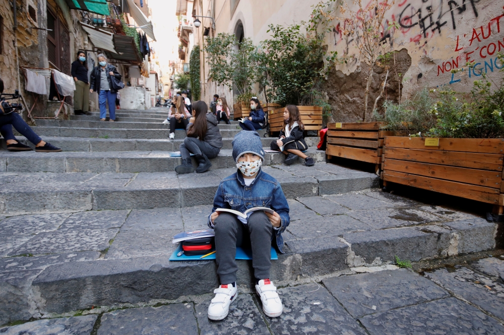 A boy wears a protective mask as Naples school teacher Pamela Buda holds her lessons to her social distancing students on public steps, after the region of Campania closed schools due to a spread of the coronavirus disease (COVID-19) in Naples, Italy, Oct