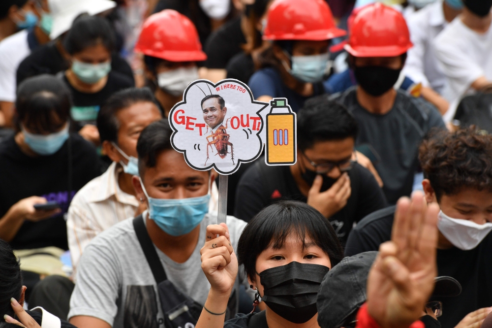 A pro-democracy protester holds a sign with the image of Thailand's Prime Minister Prayut Chan-O-Cha urging him leave office at an anti-government rally in Bangkok on October 25, 2020, as activists continued their calls for his resignation. / AFP / Mladen